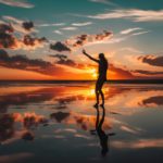 The shadow of a figure dancing on a beach with the sunset behind