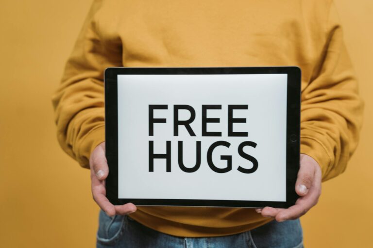 Person holding a tablet displaying 'Free Hugs' text against a yellow backdrop.